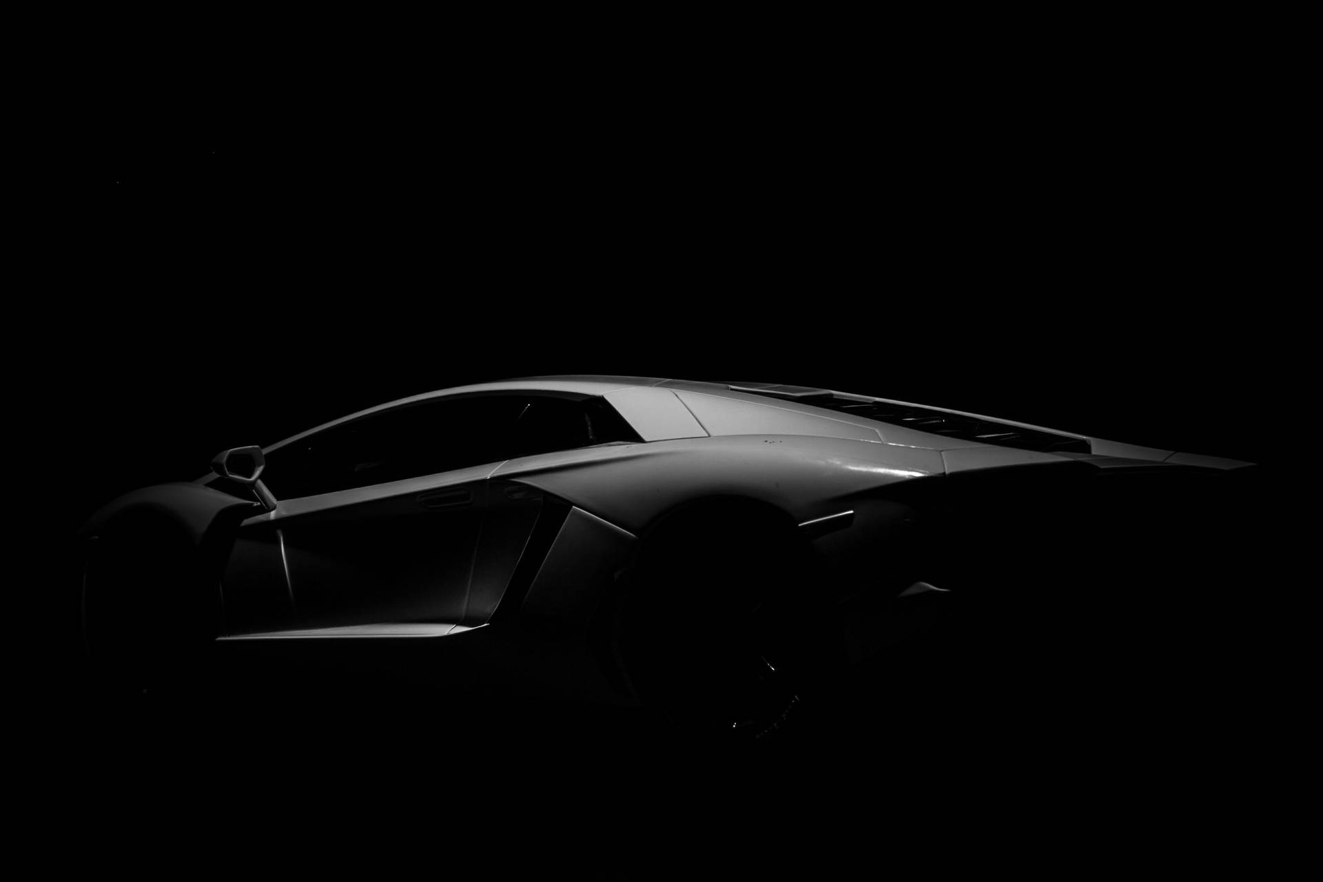 Schlanke silberne Sportwagen-Silhouette vor schwarzem Hintergrund beleuchtet — Schwarze Sportwagen Wallpaper