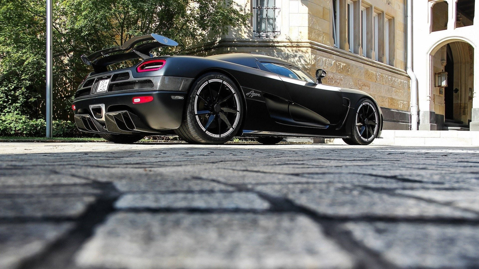 Mattschwarzer Hypercar geparkt auf Kopfsteinpflasterstraße in der Nähe eines historischen Gebäudes. — Schwarze Sportwagen Wallpaper
