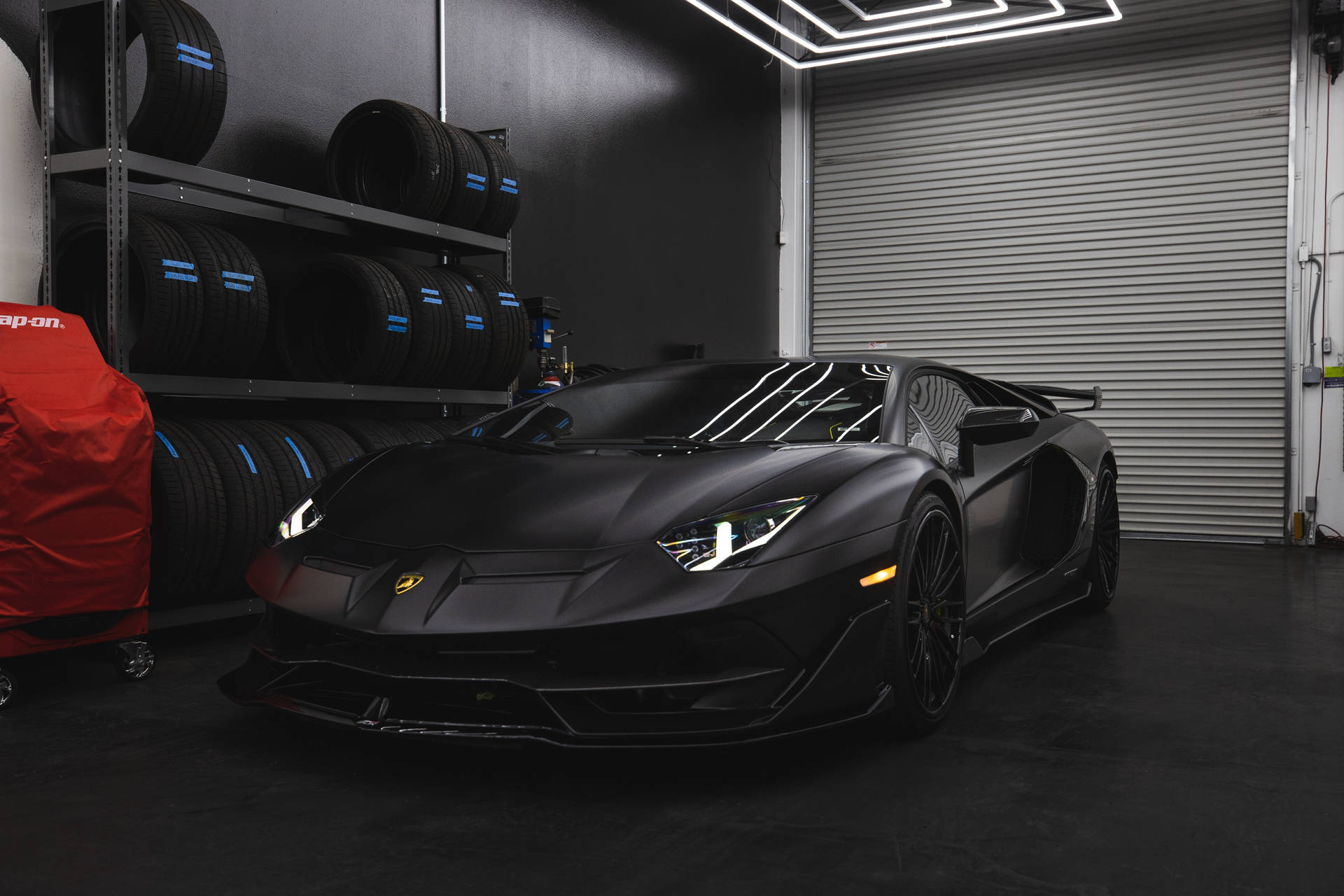 Mattschwarzer Lamborghini Aventador SVJ in einer High-Tech-Garage mit gestapelten Reifen. — Schwarze Sportwagen Wallpaper
