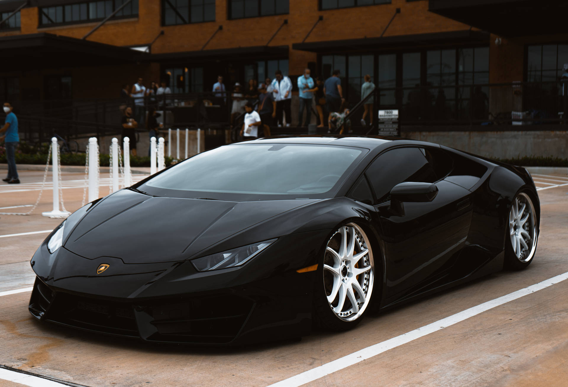 Schwarzer Lamborghini Huracán, geparkt in einer urbanen Umgebung mit Menschen in der Nähe. — Schwarze Sportwagen Wallpaper