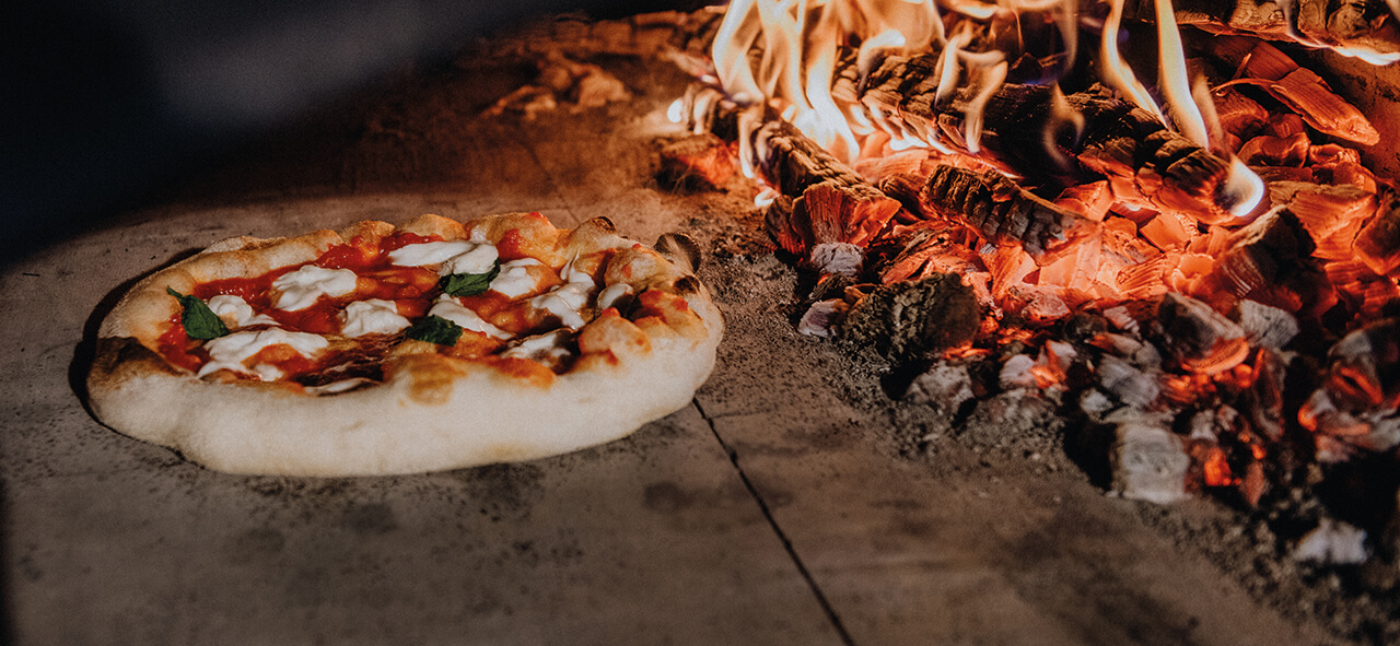 Pizza_an_der_Glut Pizza backt direkt an der Glut in einem traditionellen Holzbackofen - der Boden wird knusprig durch die intensive Hitze.