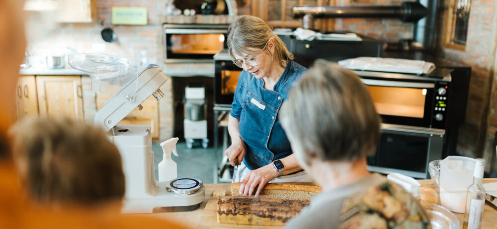 Backvorführung beim Häussler Brotfest Bäckermeisterin zeigt den Besuchern des Brotfestes bei einer Backvorführung im Backdorf, wie Teig verarbeitet wird - traditionelles Ambiente mit Elektro-Steinbackofen.