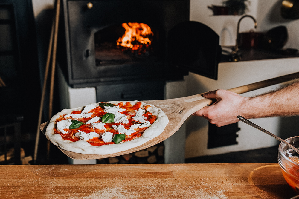 Belegte_Pizza_in_Holzbackofen Belegte Pizza wird mit einem Holzschieber in einen traditionellen Häussler Holzbackofen eingeschossen.