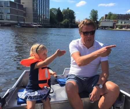 Een kind met een zwemvest en een man in een bootje wijzen naar iets op het water. Een kind met een zwemvest en een man in een bootje wijzen naar iets op het water.