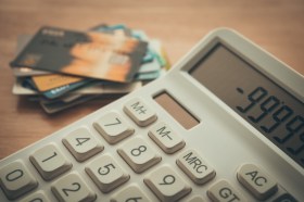 GettyImages-2225783847 White calculator shows minus delinquent and many credit cards on wooden table