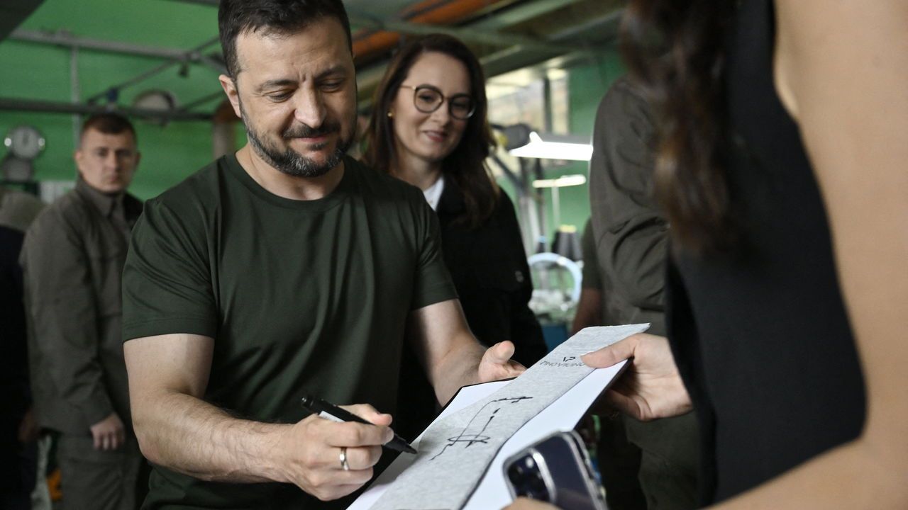 Ukrainian President Volodymyr Zelensky signs a pair of socks as a souvenir