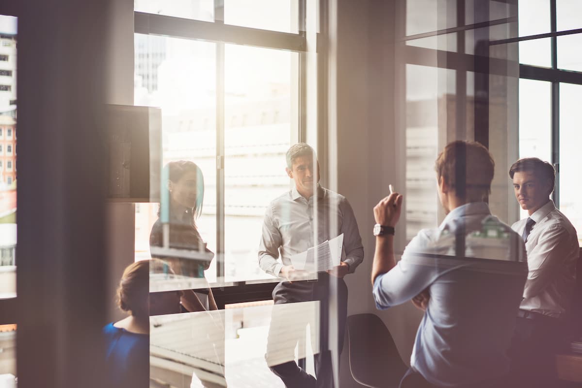 A photo of business people having discussion in board room. Male and female professionals are seen through glass. They are working in office. Business people having discussion in board room
