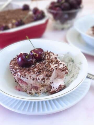 A small dish of milk jelly cherry dessert on a table with the complete serving dish in the background.