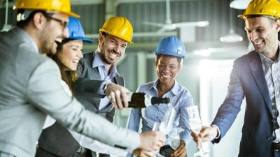 A group of people in suits and hard hats celebrate the rising share price with champagne.