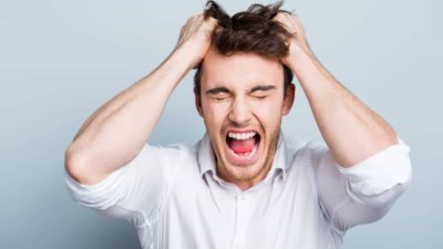 A young male investor wearing a white business shirt screams in frustration with his hands grasping his hair after ASX 200 shares fell rapidly today and appear to be heading into a stock market crash