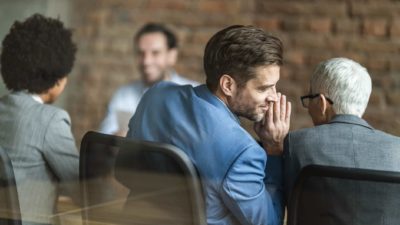 A person leans over to whisper a secret to a colleague during a meeting.