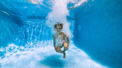 A boy plunges right to the bottom after doing a bomb into the pool.