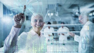 A woman researcher holds a finger up in happiness as if making the 'number one' sign with a graphic of technological data and an orb emanating from her finger while fellow researchers work in the background.