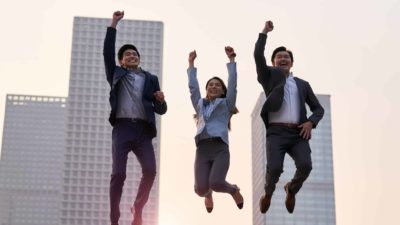 Three businesspeople leap high with the CBD in the background.