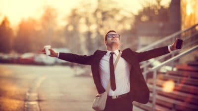 Businessman smiles with arms outstretched after receiving good news.