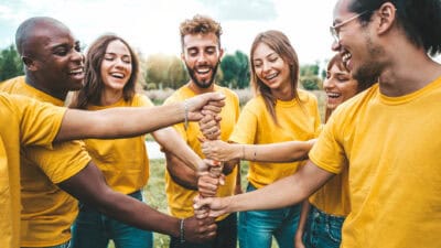 Multiracial happy young people stacking hands outside - University students hugging in college campus - Youth community concept with guys and girls standing together supporting each other.