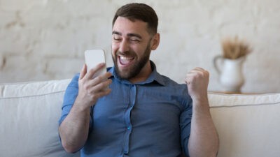 man looking happy and excited as he looks at his mobile phone