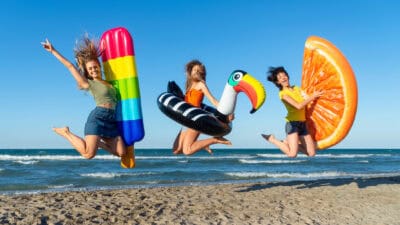 Three happy girls on jumping motion with inflatable mattresses at the beach.