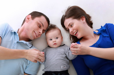 Two parents holding the hand of their baby in the middle. 