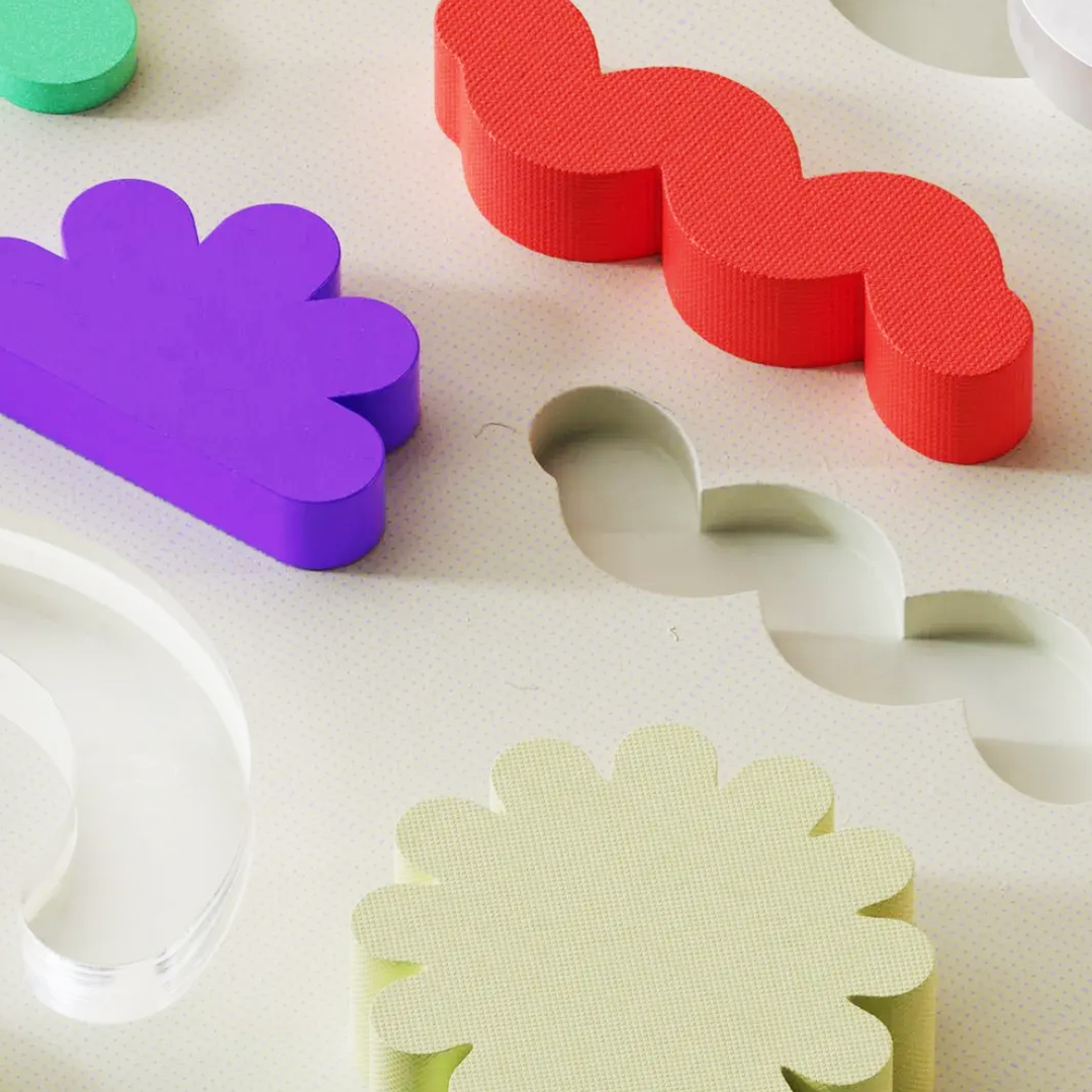 A flat surface with various shape cutouts and colorful blocks in some of the cutouts