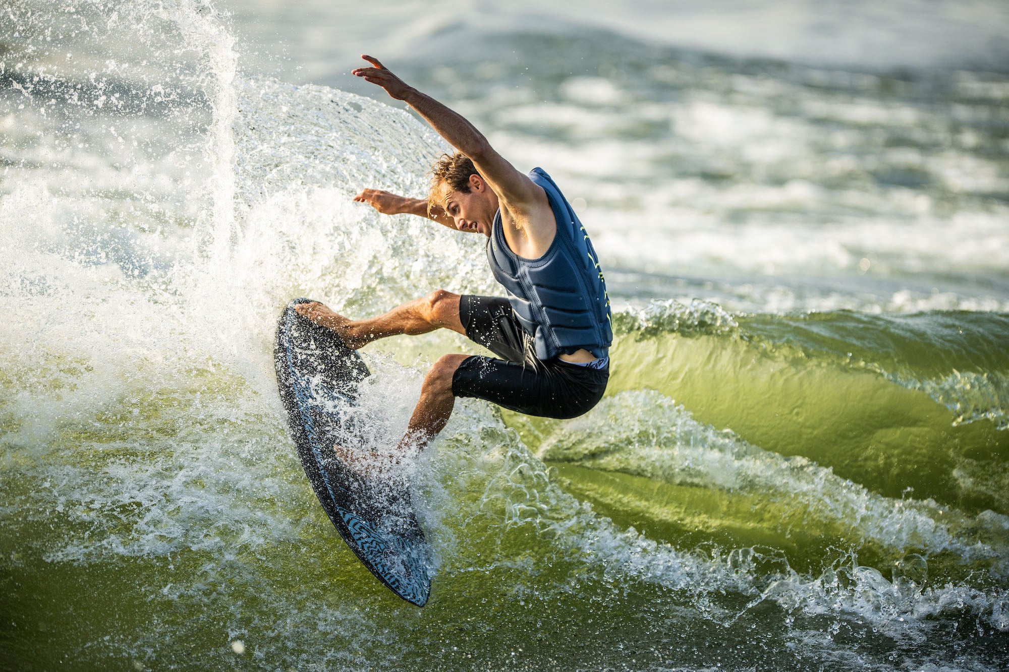 Surfer in a blue vest skillfully riding a wave, creating a splash.