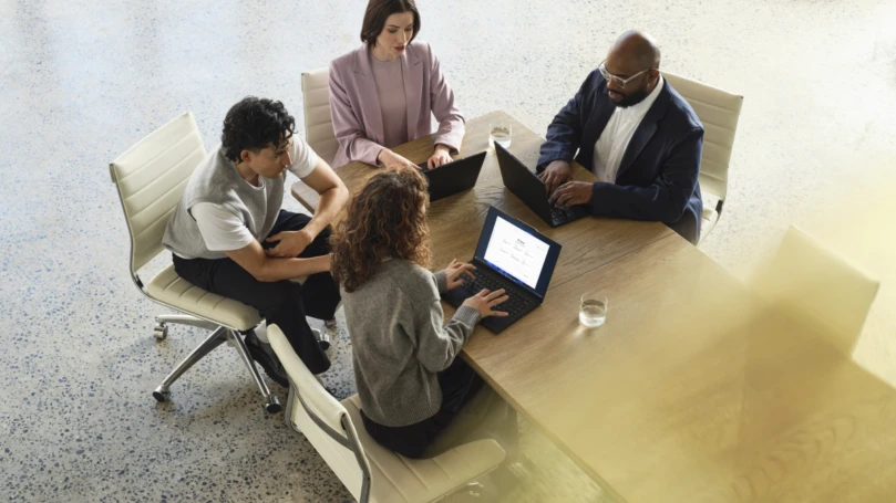 A group of people sitting around a table with laptops