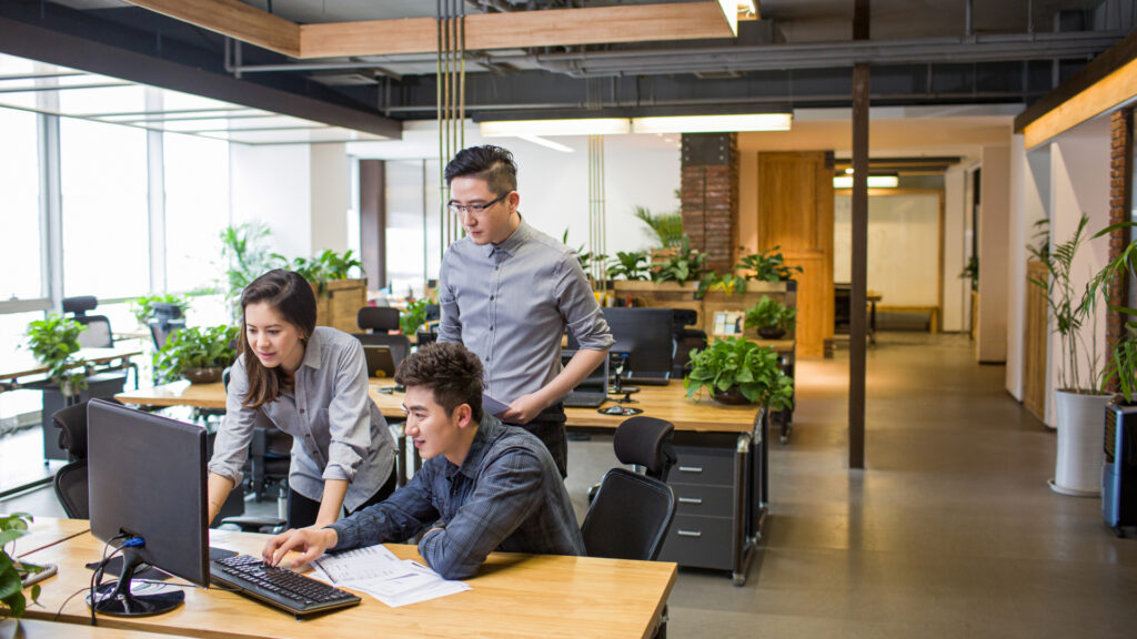 Three people working together in an office, looking at a desktop computer.