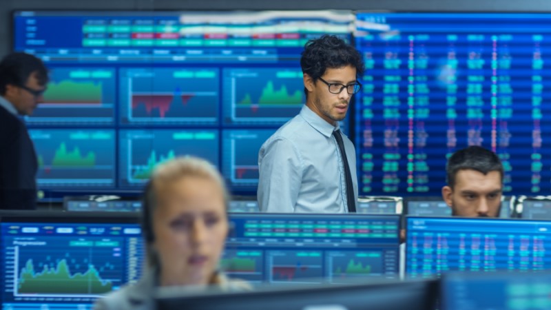 : people in room reviewing multiple screens with charts and financial information on them.