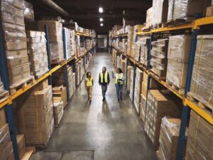 Wide shot of warehouse workers walking through the aisle with manager reviewing data real time, powered by Azure.