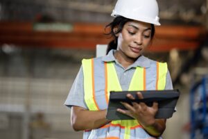 A woman wearing a hard hat and vest working on a tablet