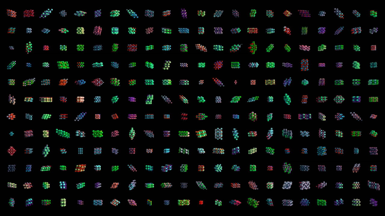 A grid of colorful, abstract shapes on a black background. Each cell in the grid features a unique three-dimensional geometric pattern, showcasing a variety of colors including green, red, blue, and purple.