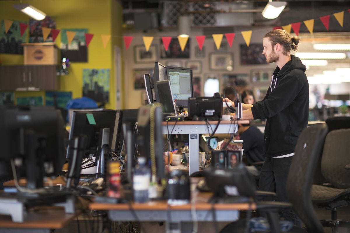 A man standing in their workstation with multiple computer screens.