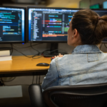 Photo of a developer coding her workspace in an enterprise office, using Visual Studio on a multi-monitor set up.