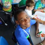 young male child coloring and pauses to smile for a photo