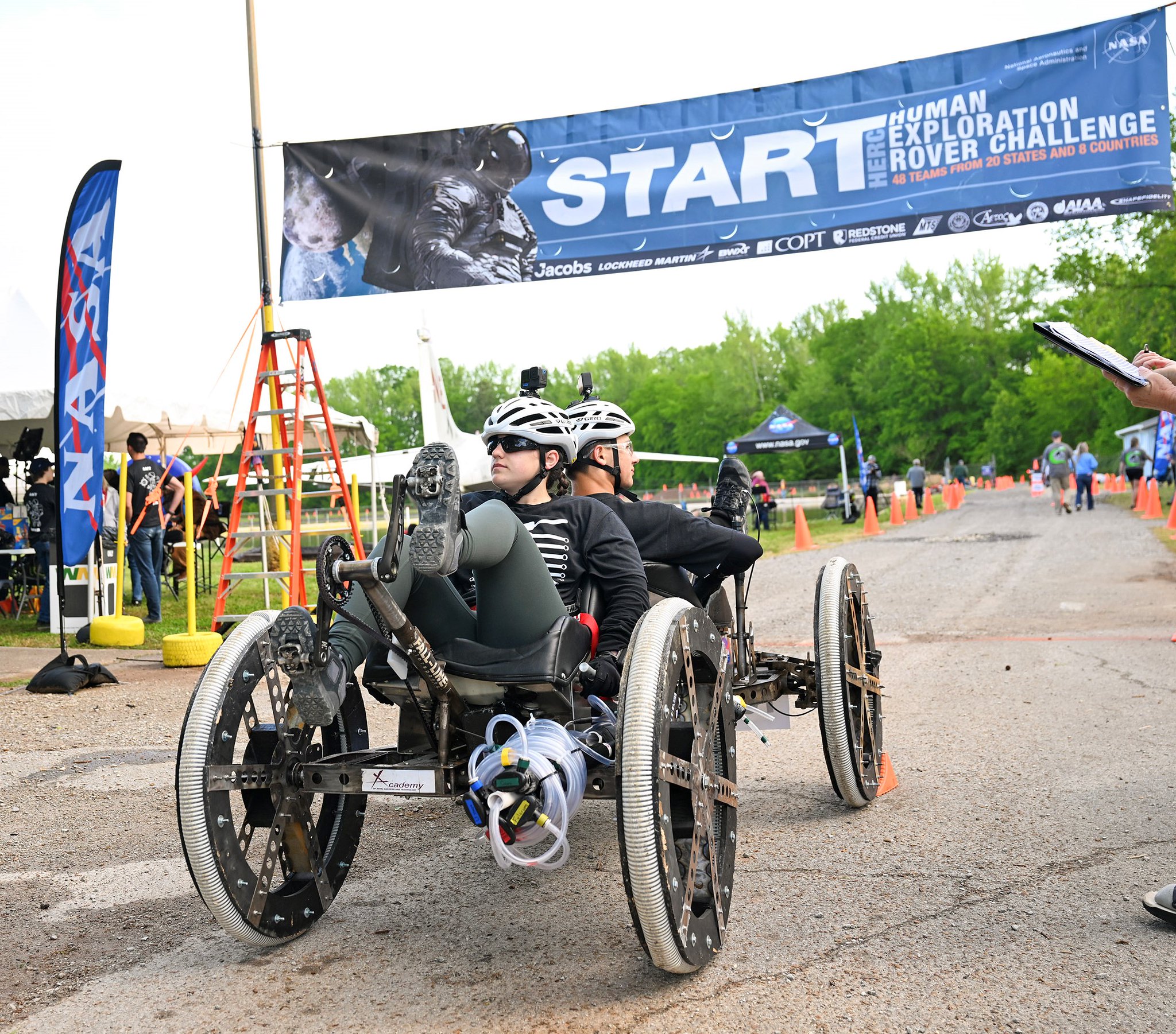 Two people on a rover challenge vehicle with a Start banner hanging above