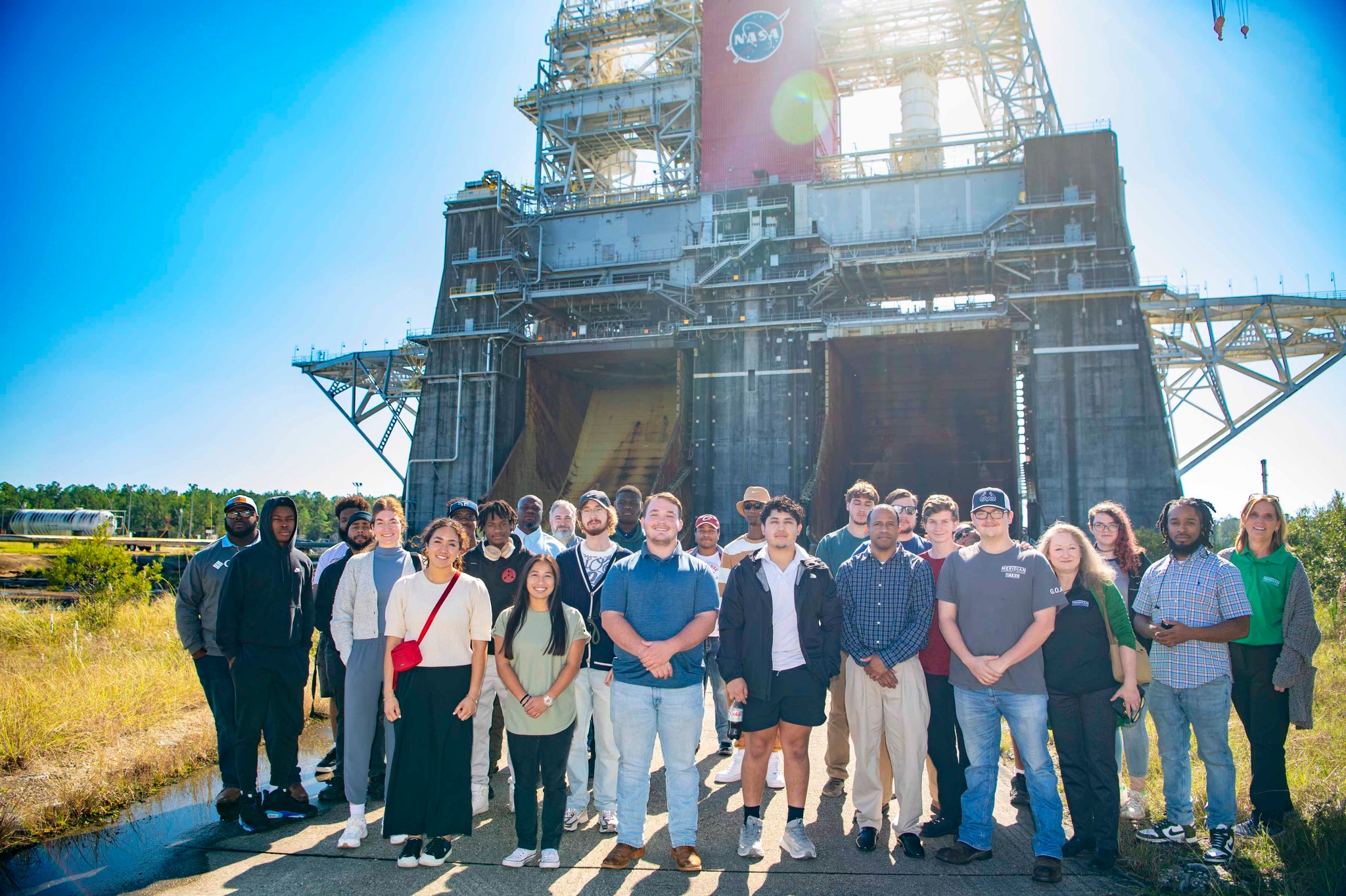 a group of college students pose for a photo in front of the Thad Cochran Test Stand while touring key facilities at NASA Stennis