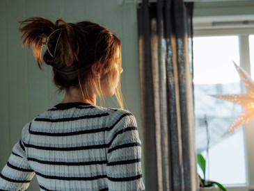 Woman admiring snowy winter view from home window with christmas star light decoration, enjoying cozy festive atmosphere