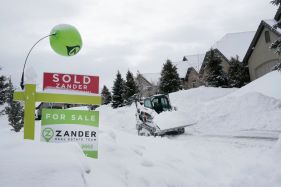 GettyImages-1247415374 A for sale sign sits in front of a house as a front end loader removes feet of snow from a residential street in Draper, Utah, on February 23, 2023. – Powerful winter storms lashed the United States on February 22, 2023, with heavy snow snarling travel across wide areas, even as unusual warmth was expected in others. Blizzards expected to dump up to two feet (60 centimeters) of snow swept across a vast band of the country from the West Coast to the Great Lakes, grounding flights and knocking out power to tens of thousands. (Photo by GEORGE FREY / AFP) (Photo by GEORGE FREY/AFP via Getty Images)