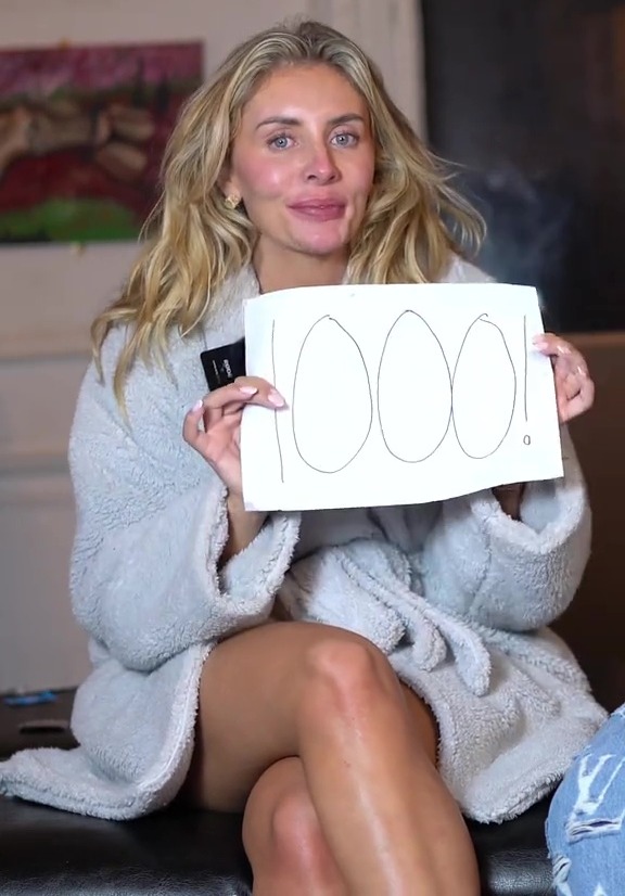 Woman in bathrobe holding sign that says 1000!