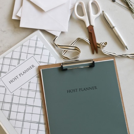 The Host Planner binder placed next to scissors, ribbon, a pen, and envelopes