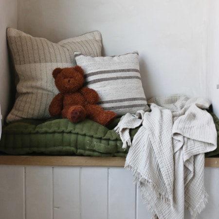 teddy bear, throw pillows, a throw blanket, and a cushion on top of a built in bench