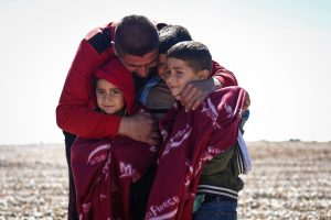 A photo of a man hugging three young boys on a beach having just got off a migrant boat.